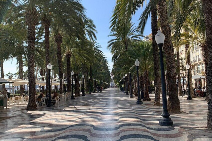 A promenade lined with palm trees and street lamps, leading towards a distant building. 2