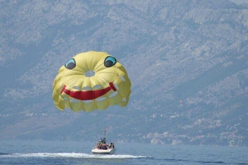 A parasail with a face design over a body of water, with a boat in the background. 5