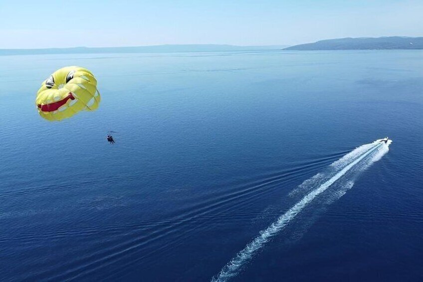 A parasailer with a yellow parachute over the ocean, a wake behind a boat, and a distant shoreline. 2