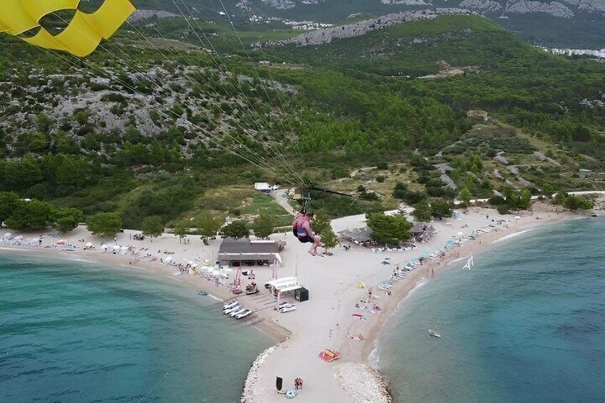 A beach with a parasail in the air, a sandy shore, and a hilly landscape in the background. 4
