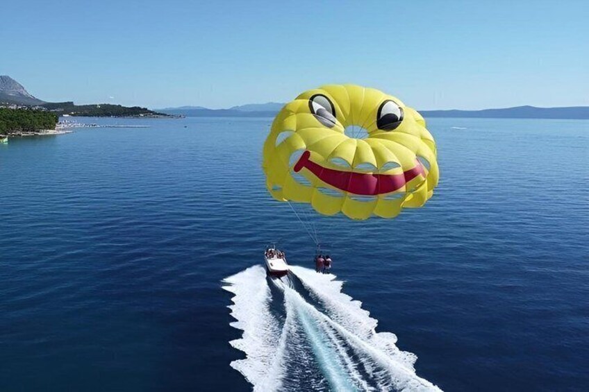 A parasail with a smiling face design over a body of water with a boat and a coastline in the background. 1