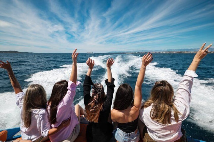 Four people on a boat with their arms raised, looking out at the sea. 2