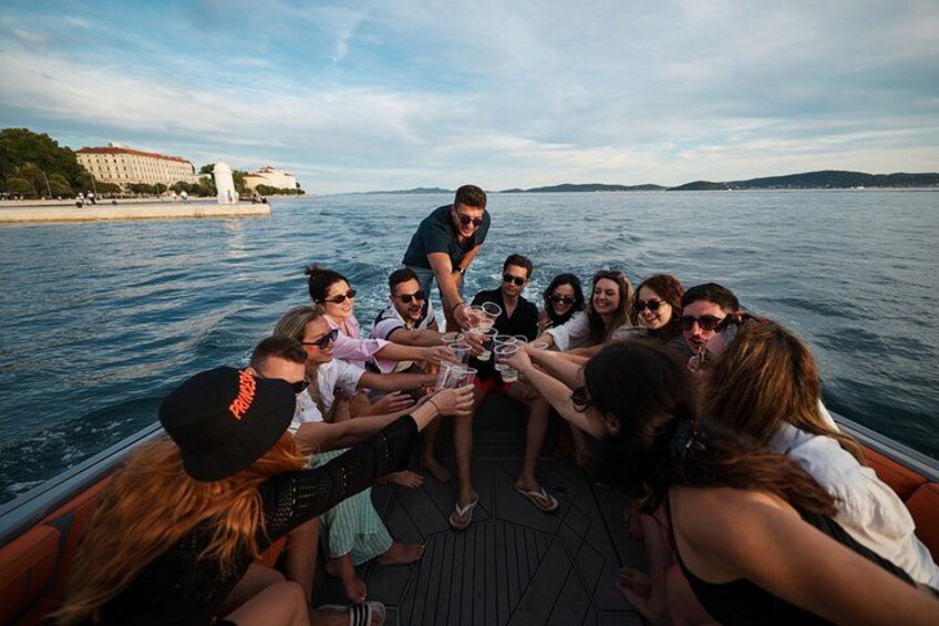 A group of people on a boat, toasting with drinks, with a body of water and a distant shoreline in the background. 4