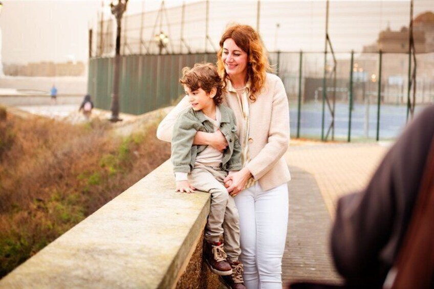 A woman and a child sitting on a concrete ledge by a waterfront. 1