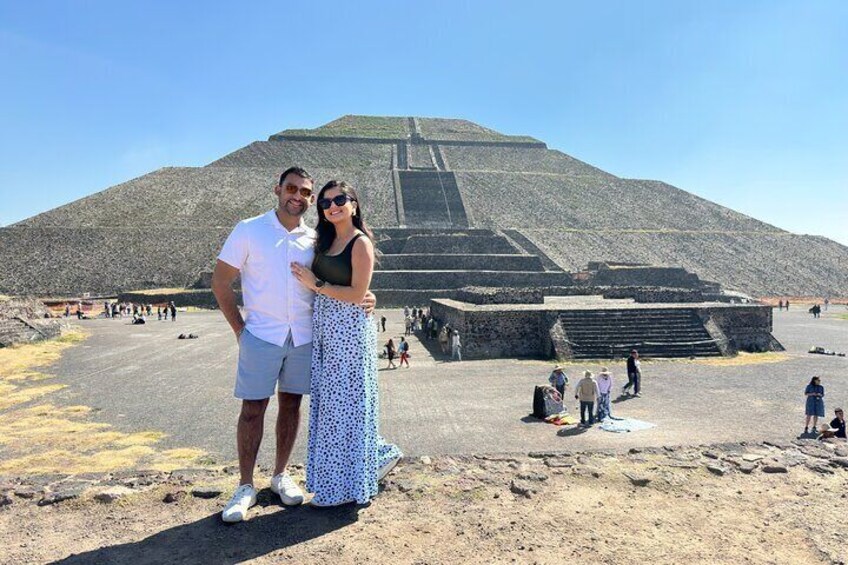 A couple posing in front of a large pyramid-like structure with a clear sky. 1