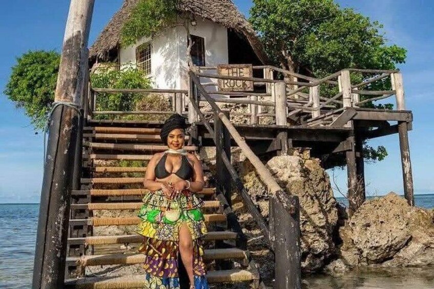 A wooden staircase leading to a thatched-roof house by the water. 1