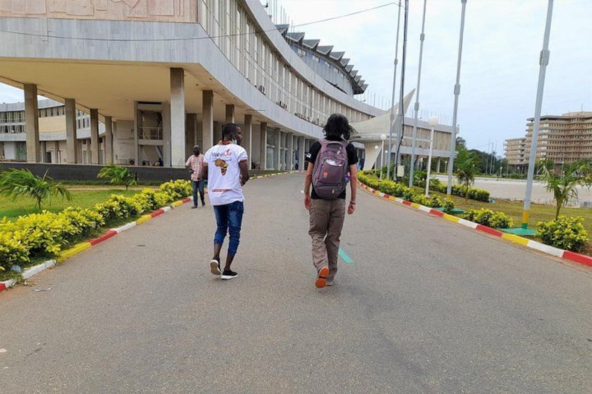 Two people walking on a paved path with a modern building in the background. 1