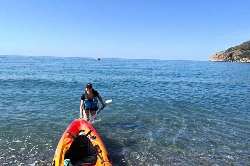 A person in a kayak on calm water, another kayak nearby, and a rocky coastline in the background. 2