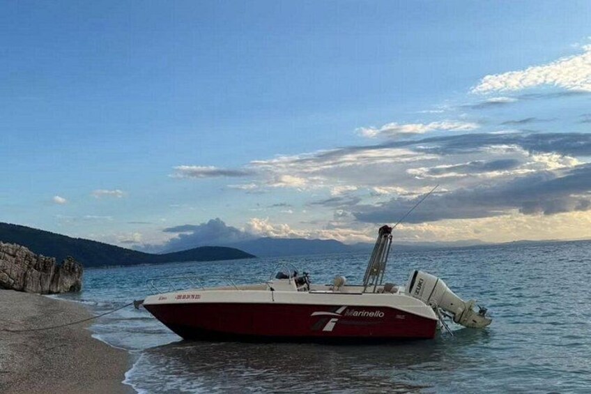A red and white boat named 'Martinello' anchored near a rocky shoreline with calm water and a distant mountain. 1