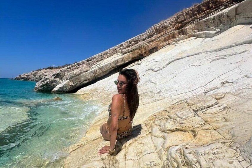 A person sitting on a rocky outcrop by the sea, with clear blue water and a white cliff in the background. 5
