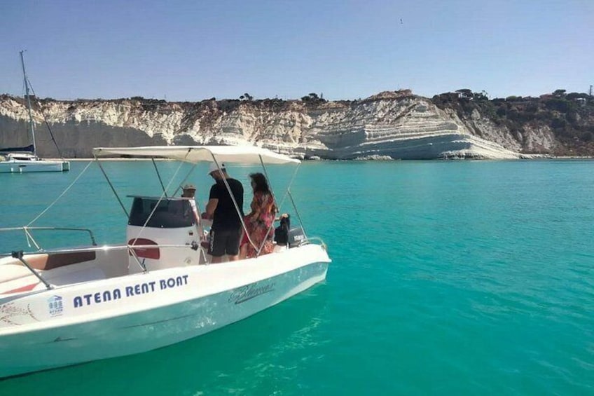 A boat with 'ATENDA RENT BOAT' written on it, a rocky coastline, and clear turquoise water. 4