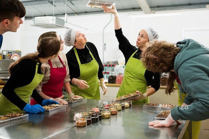 A group of people wearing aprons and hairnets, working at a stainless steel counter with jars of food items. 3