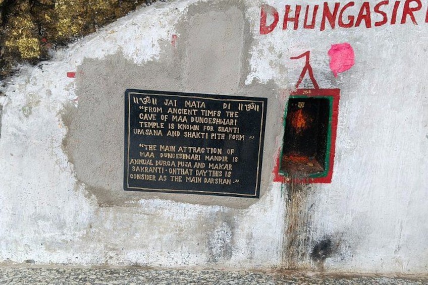 A weathered wall with a sign detailing the history of a temple, and a small window with a red frame. 3