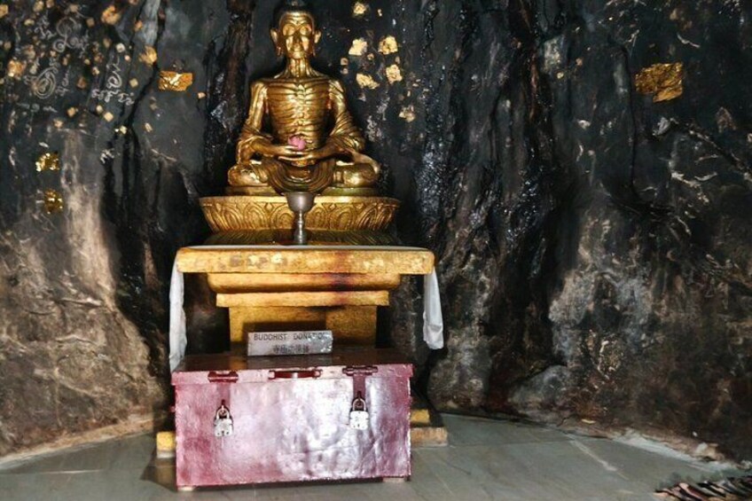A golden Buddha statue in a cave with a pink and red box in front. 2