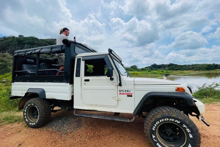 A white Bolero MANITOUCK vehicle parked on a dirt path near a body of water with a person standing in the driver's seat. 2