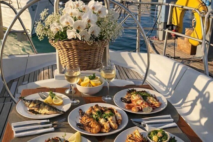 A dining table with seafood dishes, wine glasses, and a basket of white flowers on a boat. 2
