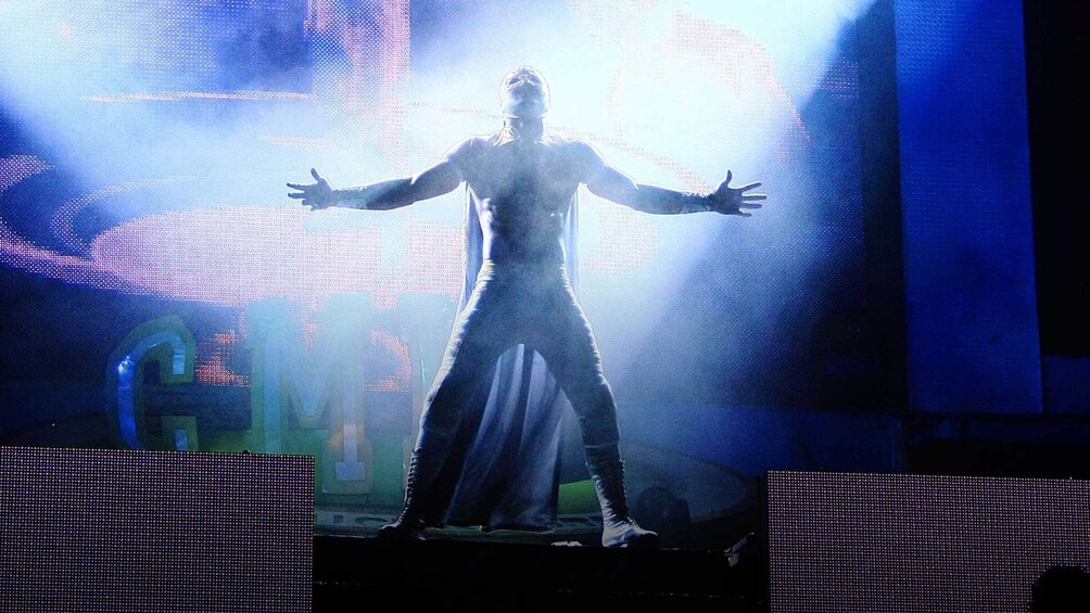 A person on stage with outstretched arms, illuminated by stage lights. 2