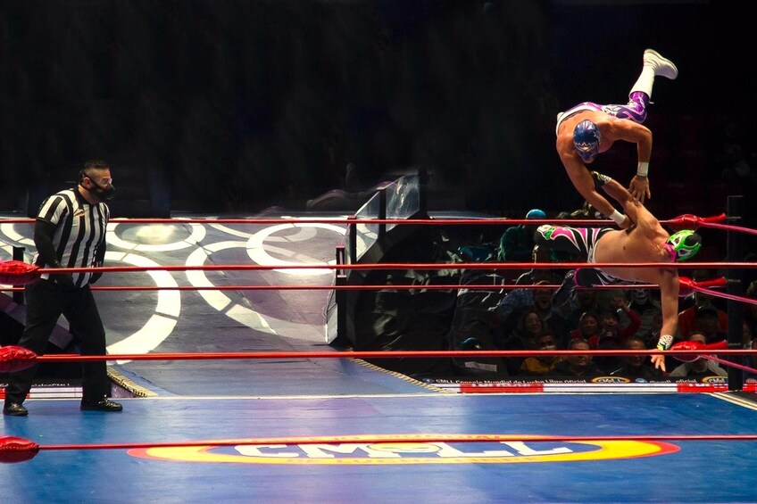A wrestling match in a ring with a referee and a wrestler performing a move. 4