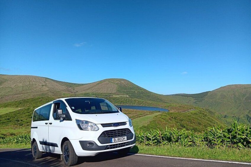 A white van on a road with a lake and hills in the background. 3