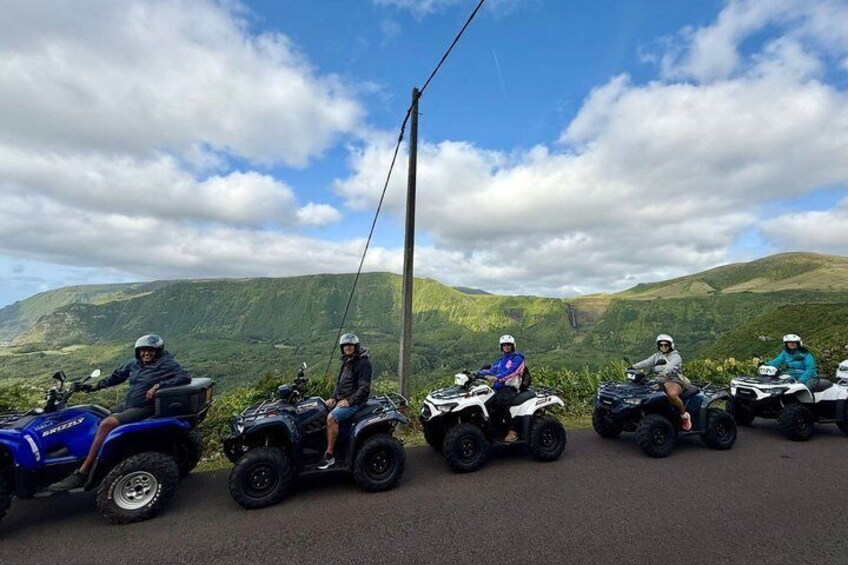 Four people on quad bikes on a road with a mountainous landscape in the background. 1