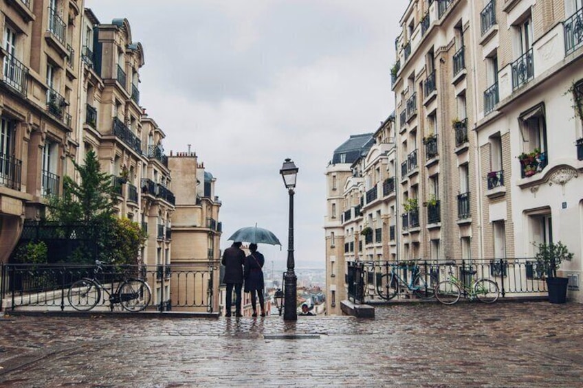 A couple walking on a wet cobblestone street with buildings on either side. 3