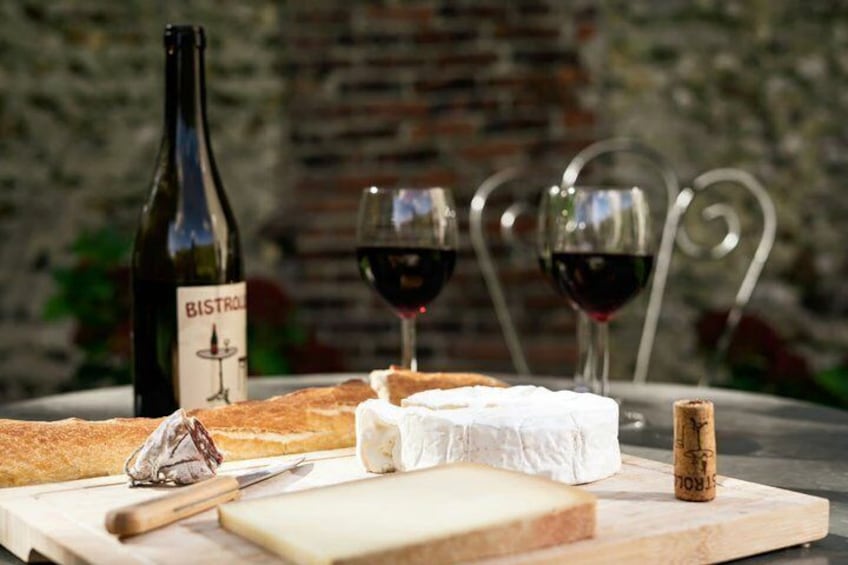 A cheese board with a bottle of Bistrone wine, two glasses of red wine, and a corkscrew on a table. 5