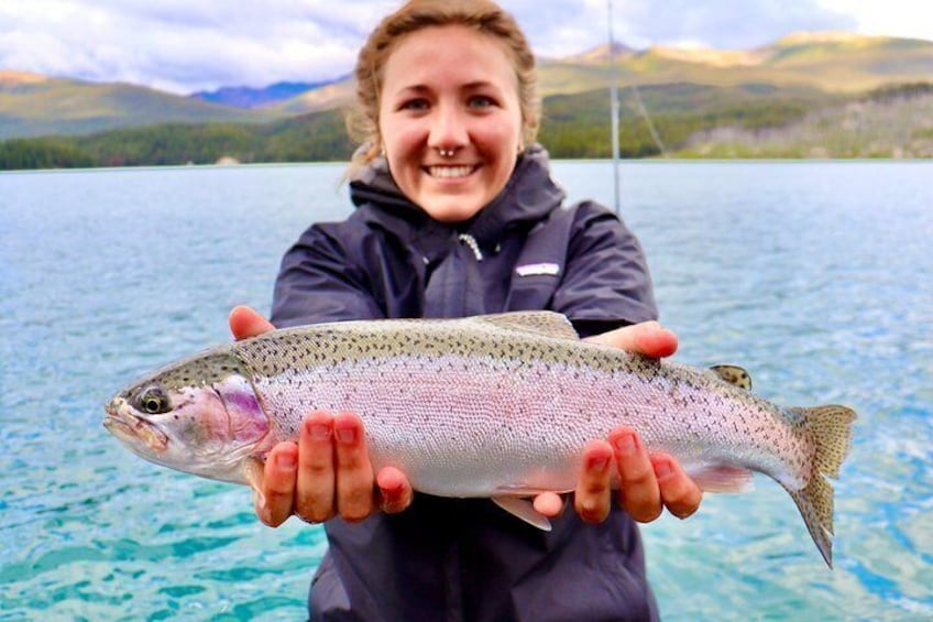 A person holding a fish by a lake with mountains in the background. 5