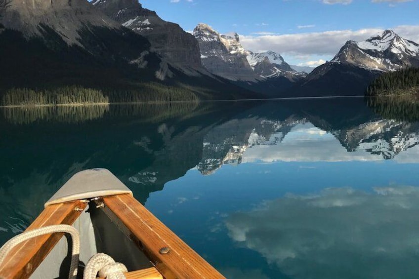 A wooden boat on a calm lake with mountains in the background. 1