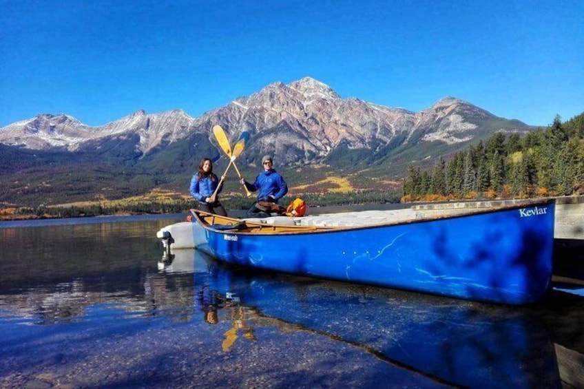 A blue boat with two people paddling on a calm lake with mountains in the background. 3