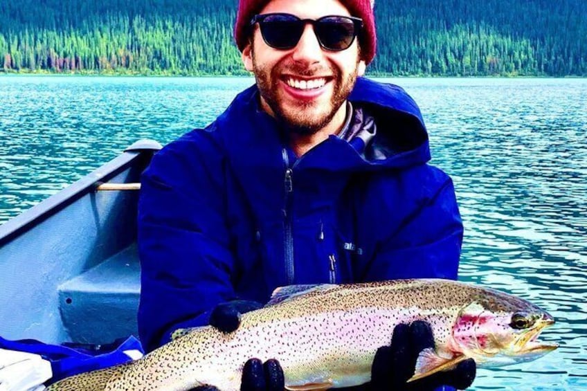 A person holding a large fish in a boat on a body of water with a forested shoreline. 4