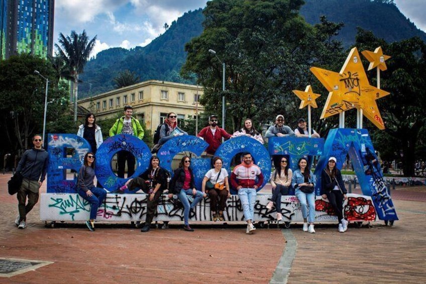 A group of people posing in front of a large, graffiti-covered number '2' structure with a star in the background. 1