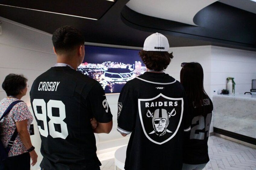 People wearing Raiders jerseys, a digital display, and a white wall. 3