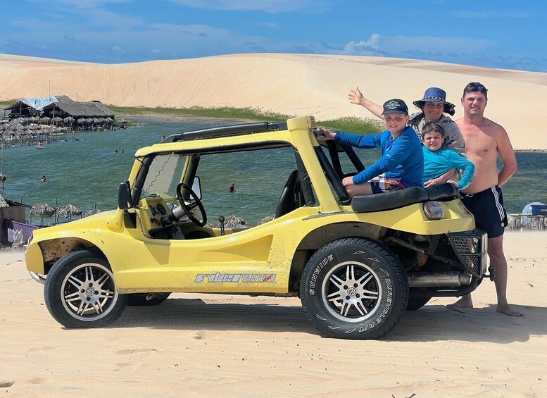 A yellow off-road vehicle parked on a sandy beach with dunes in the background. 2