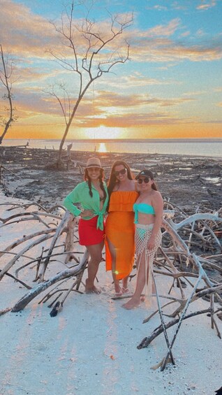 Three people standing on a beach with a sunset in the background. 3