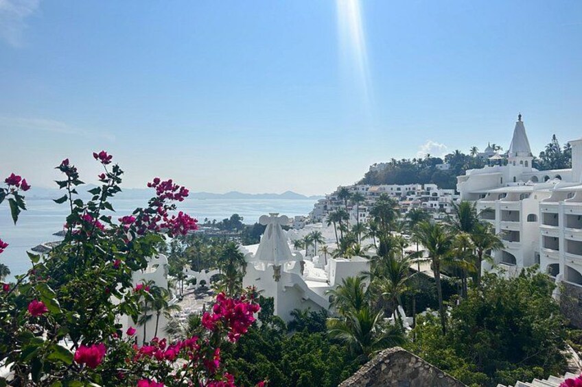 A coastal town with white buildings, pink flowers, and a clear blue sky. 5