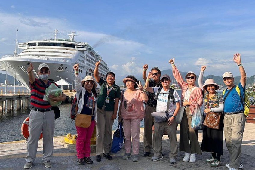 A group of people standing in front of a cruise ship at a dock. 2