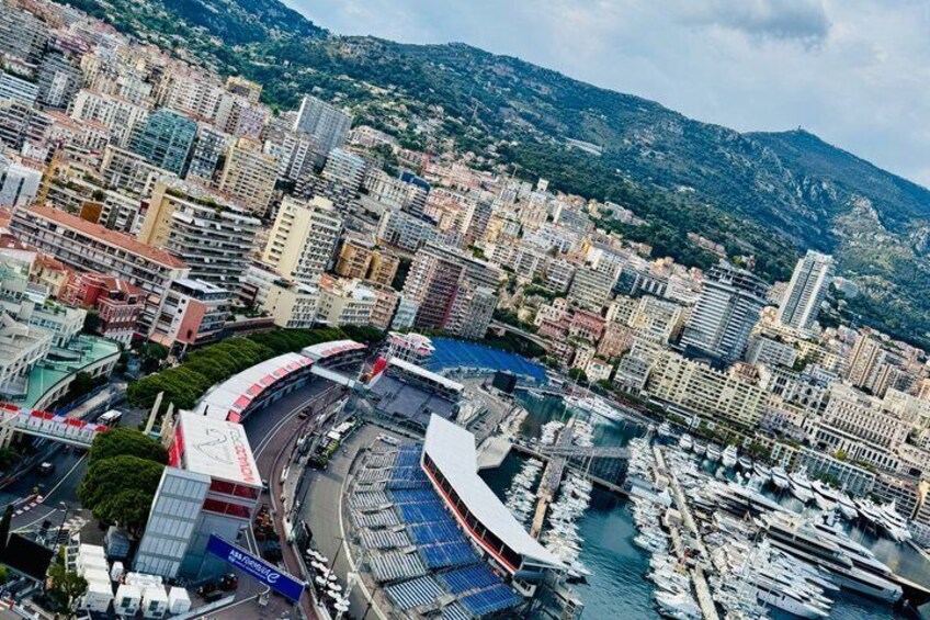 A coastal cityscape with a marina, buildings, and a mountain backdrop. 1