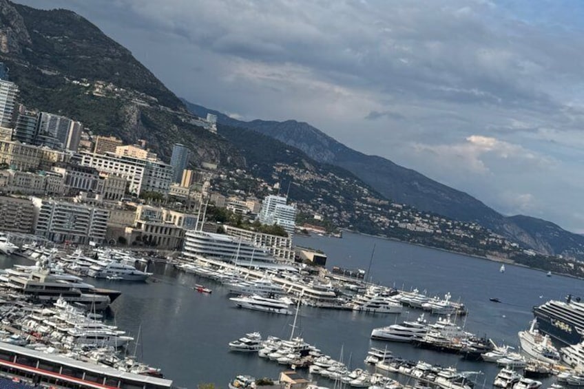 A marina with numerous boats docked, a cityscape with buildings, and mountains in the background. 5
