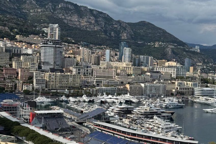 A marina with numerous boats docked, a cityscape with buildings, and mountains in the background. 3