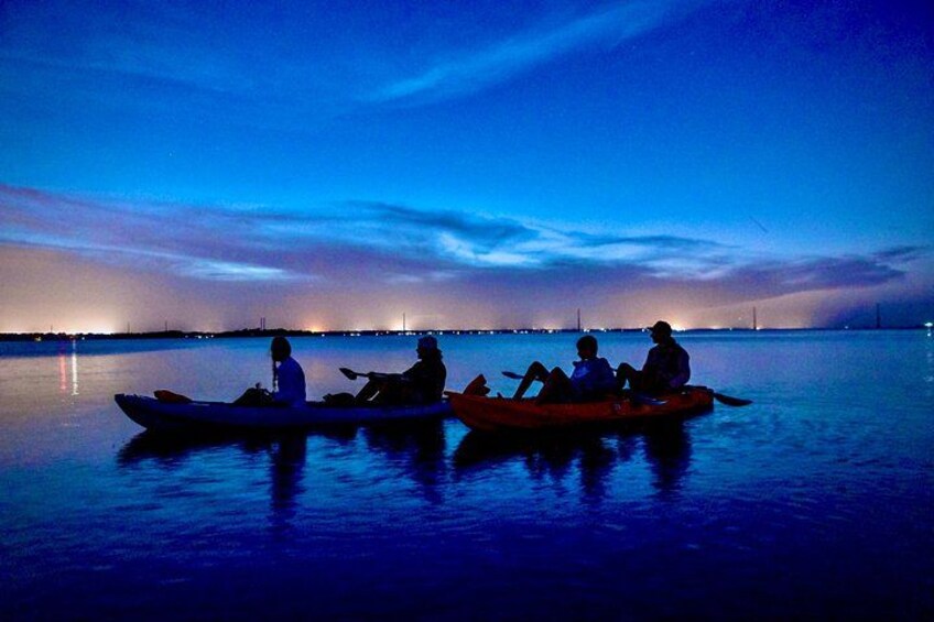 Three people in a canoe on a calm body of water at dusk. 4