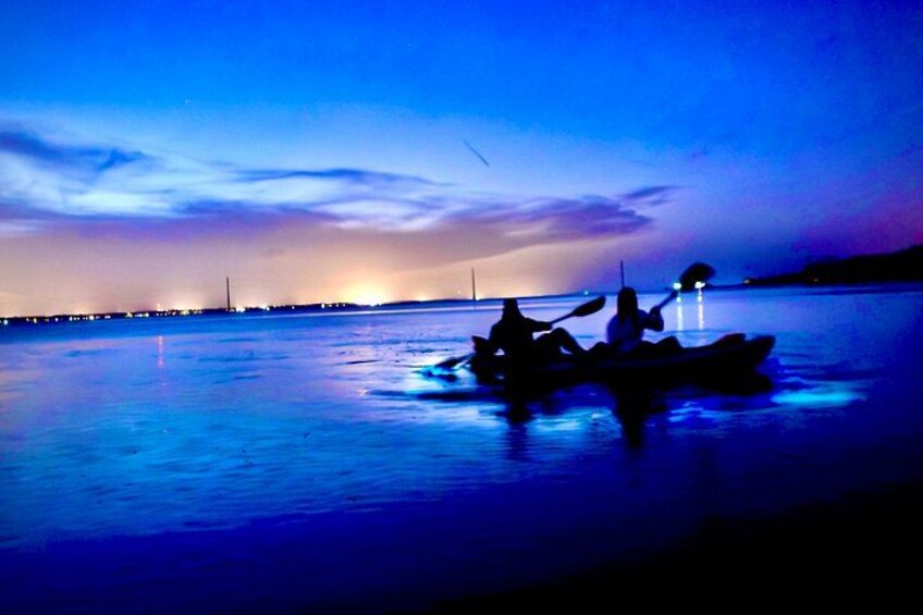 A calm body of water at dusk with a silhouette of a boat and a distant city skyline. 5