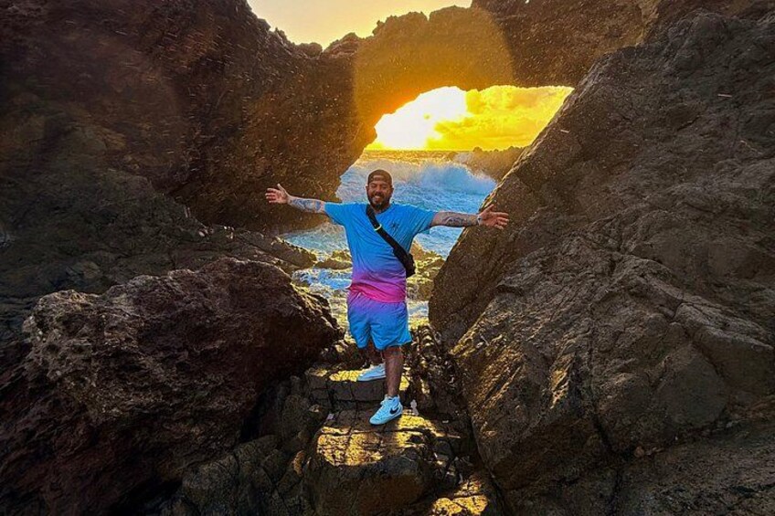 A person standing on a rock formation with arms outstretched, sun setting in the background. 2