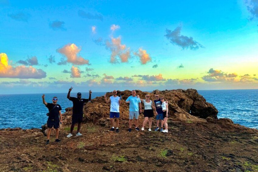 A group of people standing on rocky terrain by the ocean during sunset. 2