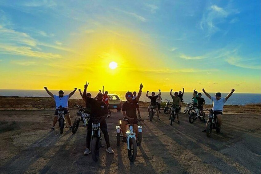 A group of people on bicycles celebrating at sunset with the sun visible in the background. 1