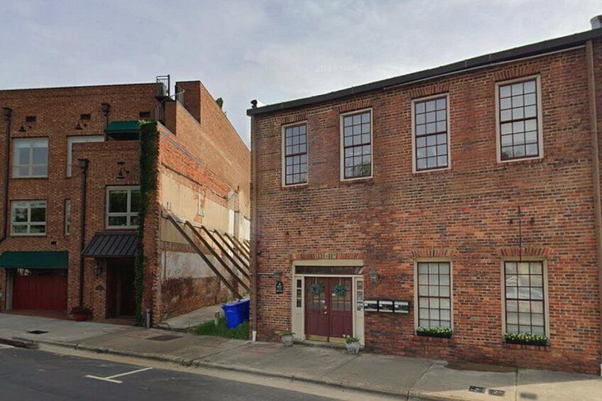 A brick building with a red door and windows, a staircase, and a blue trash bin. 5
