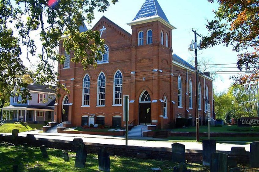 A red brick church with a steeple, arched windows, and a flagpole. 1