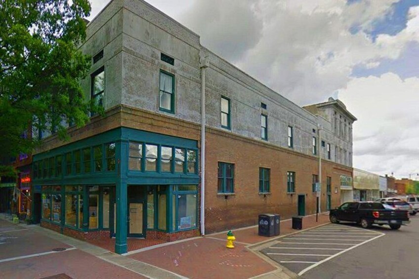 A two-story building with a green awning, a fire hydrant, and a parking lot with cars. 2