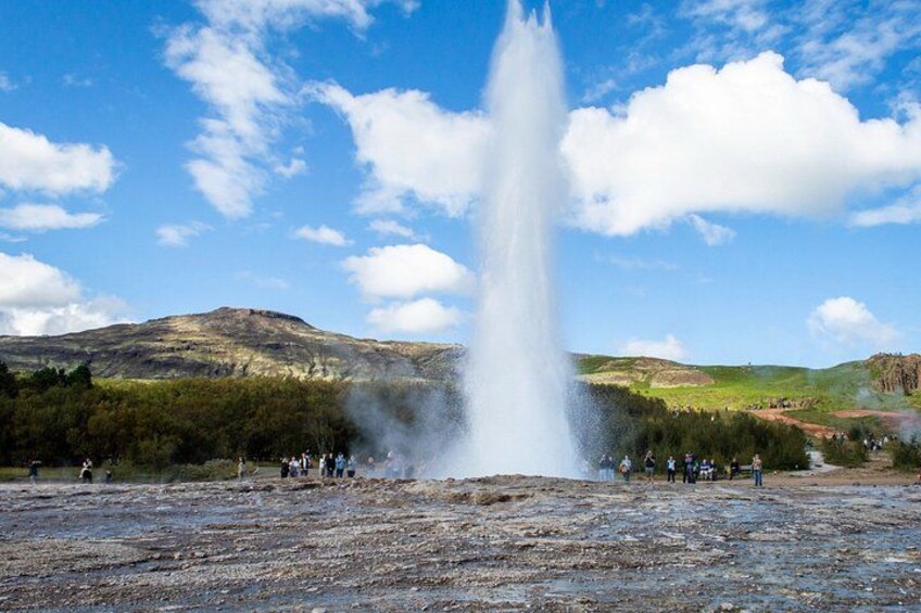 A geyser erupting with people observing in a natural landscape with hills in the background. 3