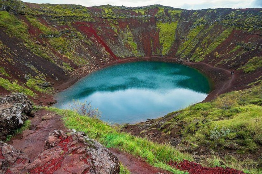 A crater lake surrounded by green vegetation and red volcanic rock. 1