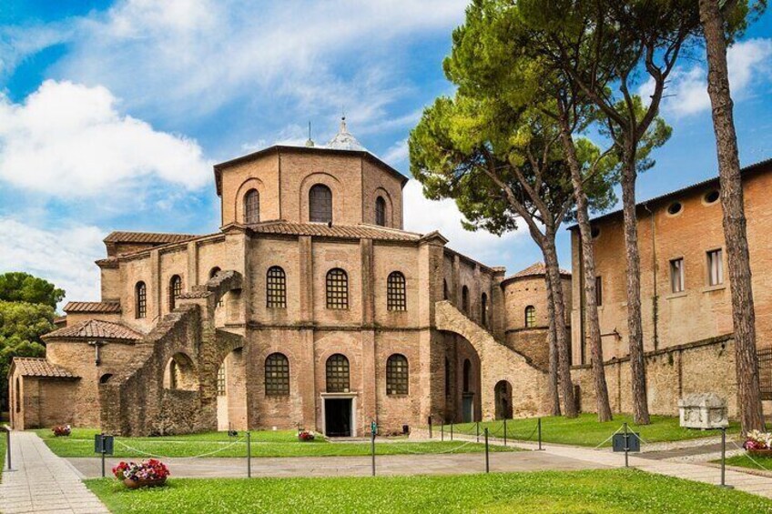 A historic building with arched windows and a central tower, surrounded by a well-maintained lawn and trees. 1